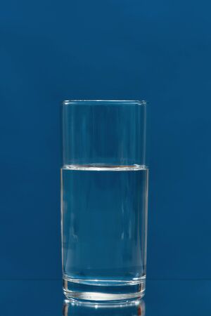 Glass of drinking water isolated on a blue background. Vertical shot