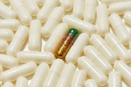 Close up of green golden glitter pill lying in the center among other white pills, capsules. Health care, creative idea and solution concept. Focus on glitter pill. Horizontal shotの写真素材
