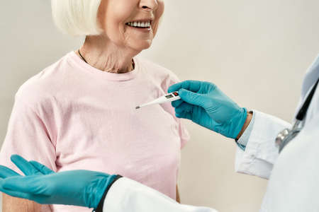 Body temperature. Doctor in blue sterile gloves using electronic thermometer for measuring...