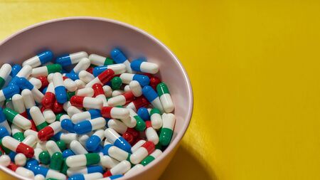 Creative concept with different medical pills, capsules lying in bowl isolated on yellow background....