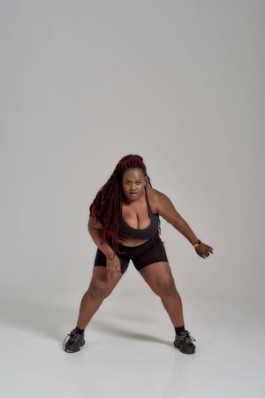 Move more. Full length shot of plump, plus size african american woman in sportswear looking at camera, dancing, posing in studio over grey backgroundの写真素材