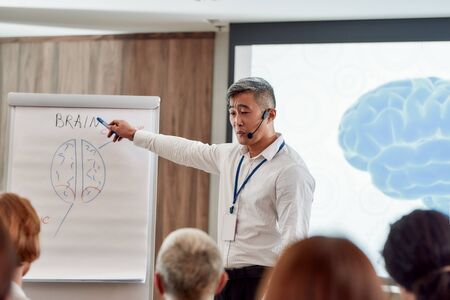 Engaging minds, empowering success. Asian male speaker in suit with headset and laser pointer giving...