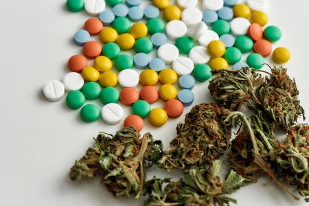Close up of medical marijuana buds and colorful pills over white background. Concept of herbal,...
