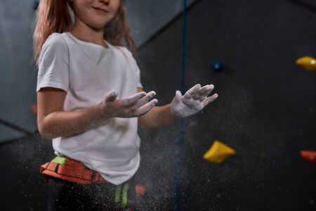 Cropped shot of sportive kid, girl applying white dust of magnesia, chalk on hands before climbing wall in bouldering center. Concept of sport life and rock climbing. Focus on handsの写真素材