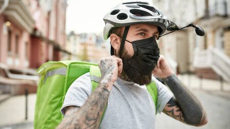 Worth relying on us. Brutal bearded delivery man in helmet wearing mask due to the emergence of the...