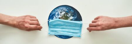 Conceptual flatlay with hands holding medical mask on planet Earth made of paper over white...