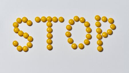 Word STOP made from yellow medical pills on light background. Stop disease. Health care and...