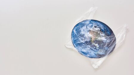 Conceptual flatlay with polyethylene plastic disposable bag covering Earth made of paper over white...