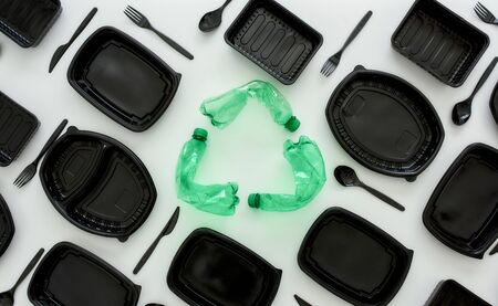 Conceptual flatlay with new empty black containers, forks, spoons and recycle symbol made of used green plastic bottles in the center. Recycling waste concept. Horizontal shotの写真素材