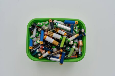 Top view of many alkaline batteries in green plastic container on white background. Concept of recycling waste and environmental pollution. Horizontal shotの写真素材