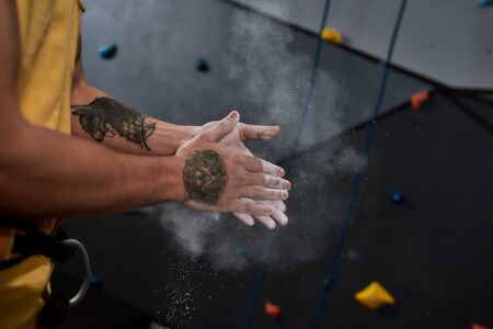 Cropped shot of sportive man applying white dust of magnesia, chalk on hands before climbing wall in bouldering center. Concept of sport life and rock climbingの写真素材