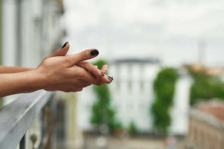 Close up shot hands of woman standing on the balcony and enjoying city view during quarantine