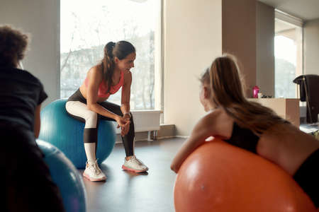 Young female trainer explaining something to kids while they are working out with exercise ball in...