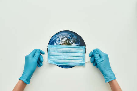 Your life, our world. Conceptual flatlay with hands in gloves holding medical mask on planet Earth...