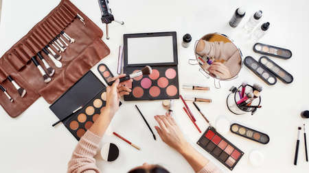 Top view of young woman, artist doing makeup, sitting at the table. Closeup female hands applying...