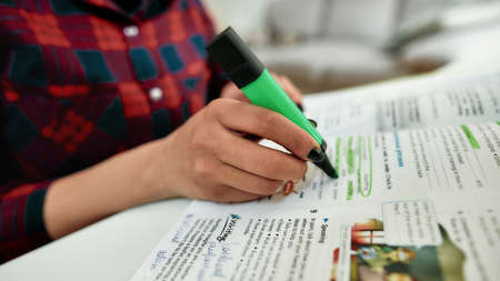 Homework. Cropped shot of a female student learning English, studying at home. Making some notes in...