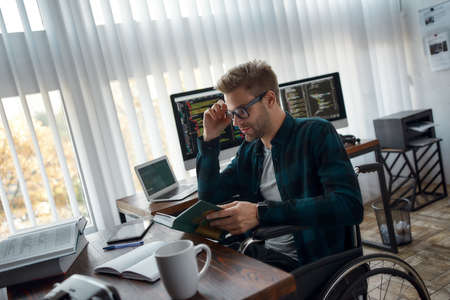 Successful people never stop learning. Side view of young male web developer in a wheelchair reading...