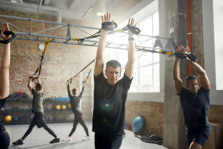 Fit Results. Athletic young man doing fitness training exercises at industrial gym. Push-up, group workout conceptの写真素材