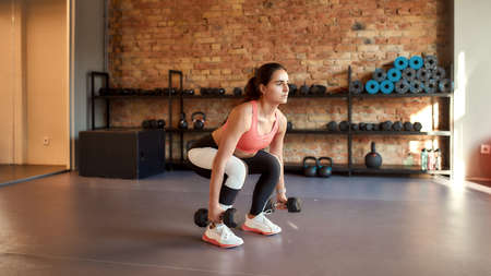 Full length shot of young athletic woman working out using dumbbells in gym. Sport, healthy...