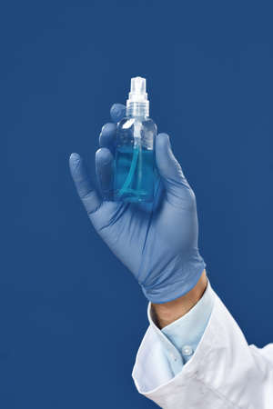 Stay safe. Cropped shot of male doctors hand in blue sterile gloves holding antiseptic gel or hand sanitiser, isolated against navy blue background. Healthcare and hygiene. Coronavirus preventionの写真素材