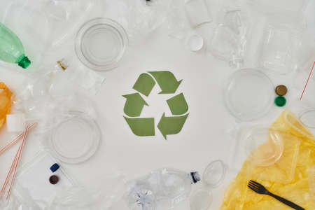 All about recycling. Flatlay composition with different empty plastic bottles, containers and recycling sign made of paper in the center over white backgroundの写真素材