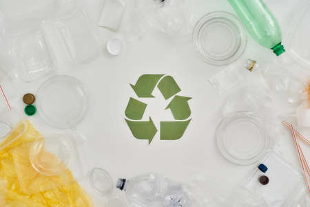 Flatlay composition with different empty plastic bottles, containers and recycling sign made of paper in the center over white backgroundの写真素材