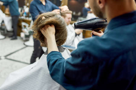Back view of barber drying long hair of his client sitting in armchair in the modern barber shopの写真素材