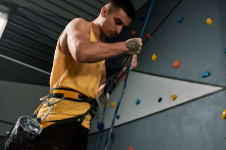 Young sportive man, rock climber holding rope, ready for training on the artificial climbing wall. Concept of sport life and climbingの写真素材
