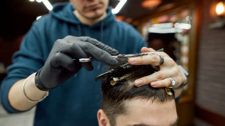 Getting modern haircut. Close up shot of professional male barber making haircut for his client, working with scissors and hair combの写真素材