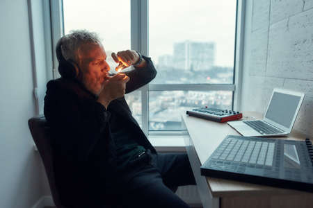 Cannabis and weed legalization concept. Bearded middle-aged man, artist or music composer lighting up joint while making songs in home studioの写真素材