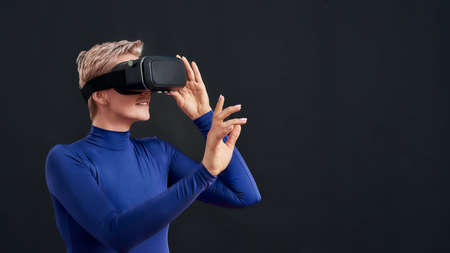 Woman with short hair in blue turtleneck wearing virtual reality headset, vr glasses isolated over dark backgroundの写真素材