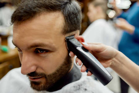 Close up shot of a young handsome bearded man getting trendy haircut while visiting barbershop....