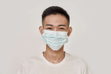 Mask on. Portrait of young asian man wearing medical mask, smiling at camera isolated over white...