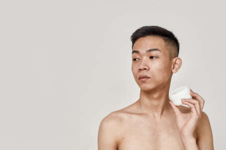 Look good. Portrait of shirtless young asian man with clean shaven face holding cream jar, advertising skincare product isolated over white background. Beauty, skincare routine conceptの写真素材