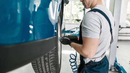 Cropped shot of male mechanic screwing or unscrewing car wheel of lifted automobile by pneumatic wrench at auto repair shopの写真素材