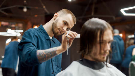 Young hipster guy getting new trendy haircut in the modern barbershop. Professional barber cutting...