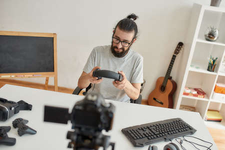 Male technology blogger holding headphones, looking dissatisfied while recording video blog or vlog about new gadgets at home studioの写真素材