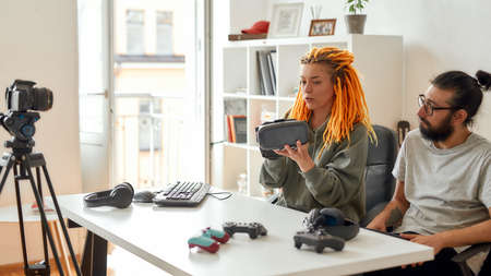Woman with dreadlocks holding vr glasses. Young male and female technology blogger recording video blog or vlog about new gadgets at homeの写真素材