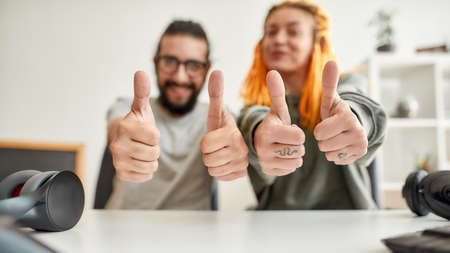 Cheerful man and woman showing thumbs up at camera. Young male and female technology blogger recording video blog or vlog about new gadgets at homeの写真素材
