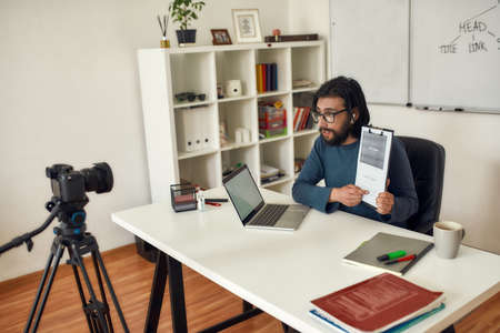 Young man in eyeglasses recording video blog about HTML on professional digital equipment, teaching...