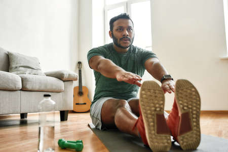 Do your best. Young active man watching online video training during morning workout with dumbbells...