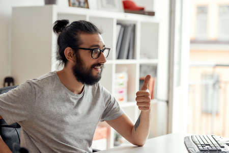 Close up of male blogger showing thumbs up, while recording video blog or vlog at home studio