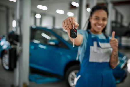 It is done. Young african american woman, professional female mechanic smiling at camera, giving car...