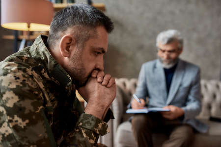 Need help. Middle aged military man looking thoughtful during therapy session with psychologist. Soldier suffering from depression, psychological trauma. PTSD conceptの写真素材