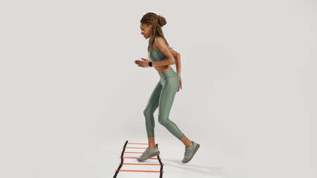 Move forward. Full length shot of young sportive mixed race woman in sportswear training on agility...