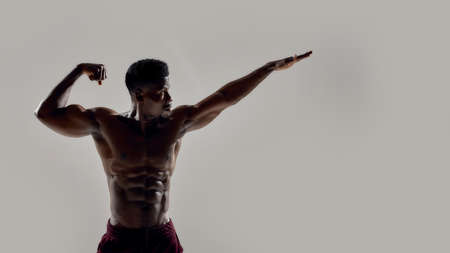 Strength inside and out. Young muscular african american bodybuilder looking aside, posing shirtless isolated over grey background. Sports, workout, bodybuilding conceptの写真素材