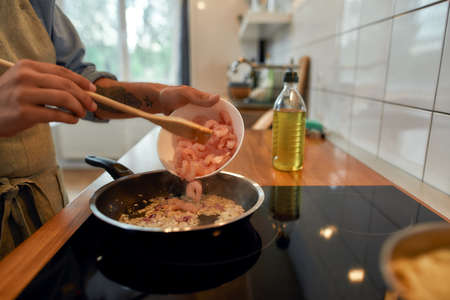 Close up of man adding shrimp to sauteed garlic and onion in the frying pan. Cook preparing dish...