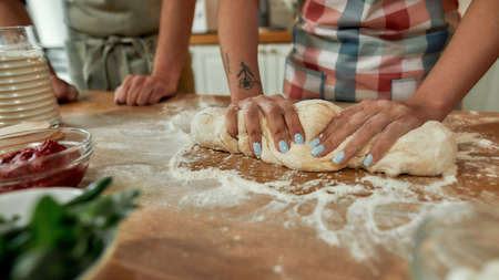 Cropped shot of couple making pizza together. Woman in apron kneading the dough while man helping...
