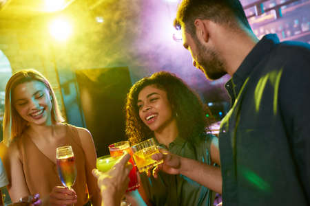 A group of friends, young women and man chatting while having fun, drinking cocktails, spending time together in the night club