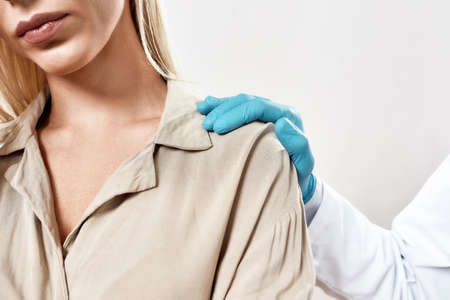 Visiting doctor. Cropped studio shot of a doctor in blue sterile gloves supporting upset female patient standing against grey backgroundの写真素材